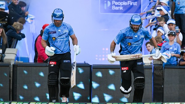 Two Adelaide Strikers players in front of a People First Bank logo.