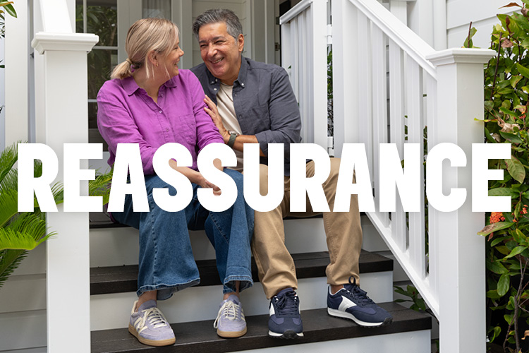 A couple sitting on the steps of a white weatherboard house with the word "REASASSURANCE" overlayed