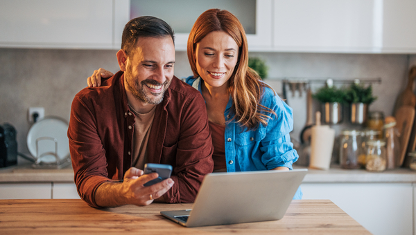 Couple at kitchen bench smiling at laptop.