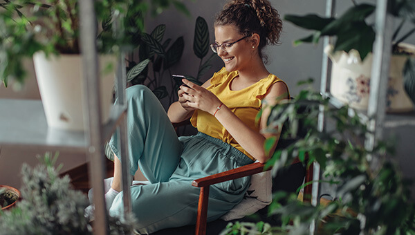 A woman sits surrounded by plants, checking her phone.