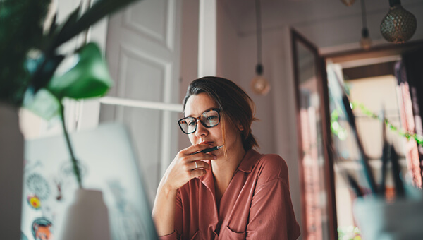 Woman pauses to think at her desktop in a sunny home office. 