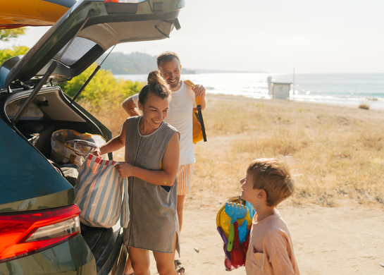Parents and their young son, unpacking a car near a beach.