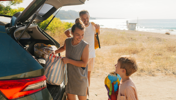 Parents and their young son, unpacking a car near a beach.