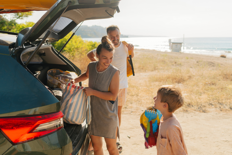 Parents and their young son, unpacking a car near a beach.