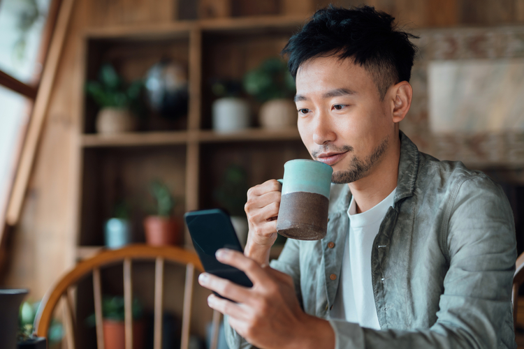 Man sipping tea while checking his phone.