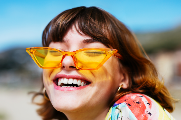 Woman in yellow tinted sunglasses smiling.