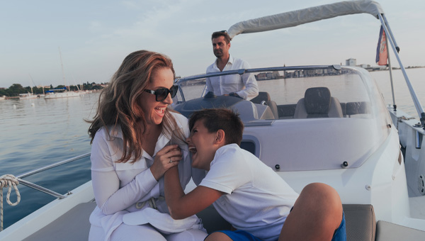 Three people on a boat with water and shoreline in background.