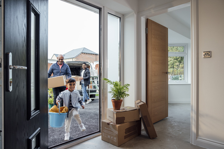 Family moving into new home with boxes and plant near open front door.