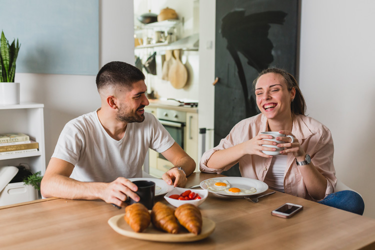 Two people having breakfast with croissants and coffee at a table.