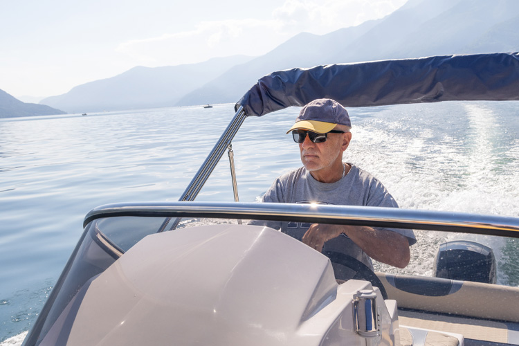 Person steering boat on water with mountains in background.