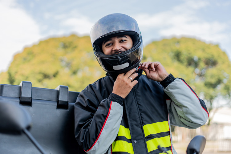 Person wearing helmet and reflective jacket adjusting helmet strap on motorcycle.