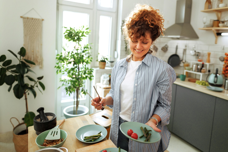 Person holding plate of food in kitchen with plants and utensils in background.