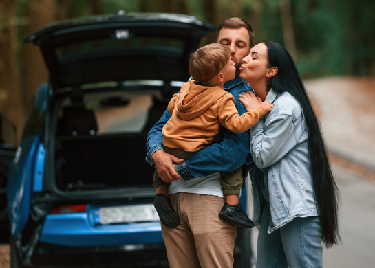 Young family hugging in forest road trip.