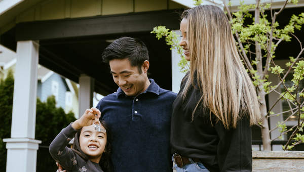 Couple with young child outside house.