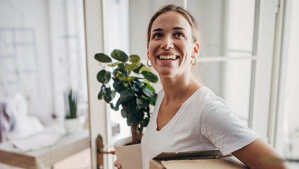 Woman carrying plant and boxes into new home.