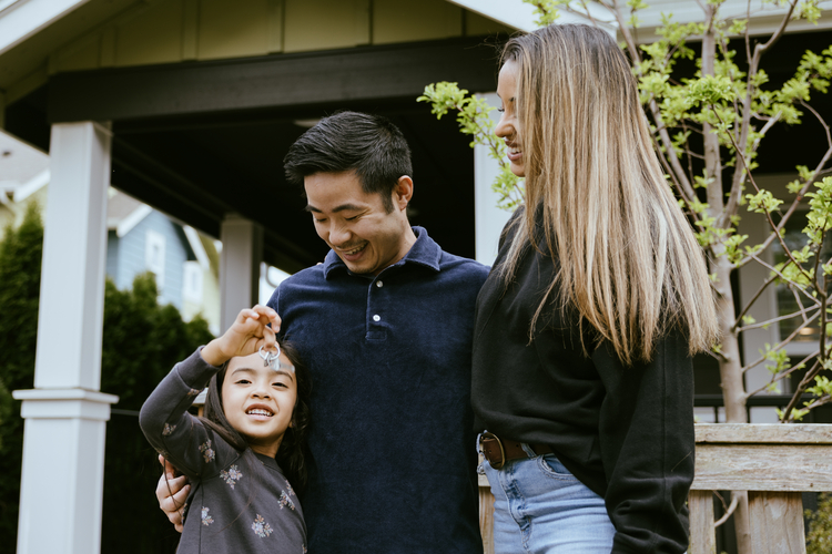 Couple with young child outside house.