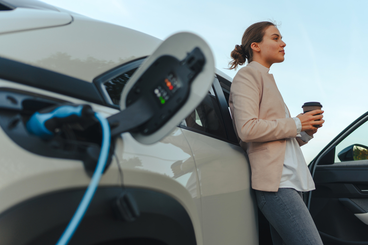 Woman drinking coffee while charging her car.