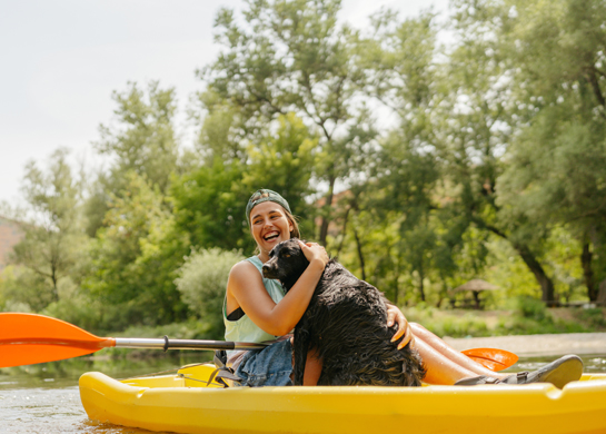 A woman cuddles a dog while on a kayak.
