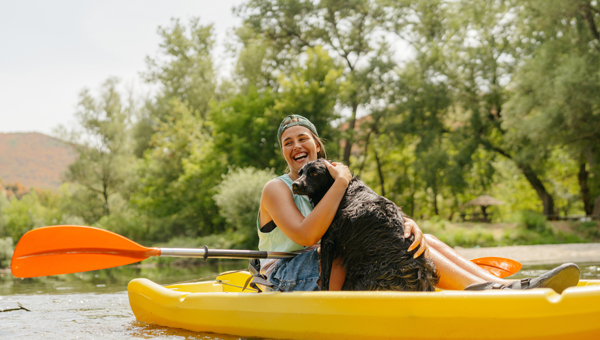 A woman cuddles a dog while on a kayak.
