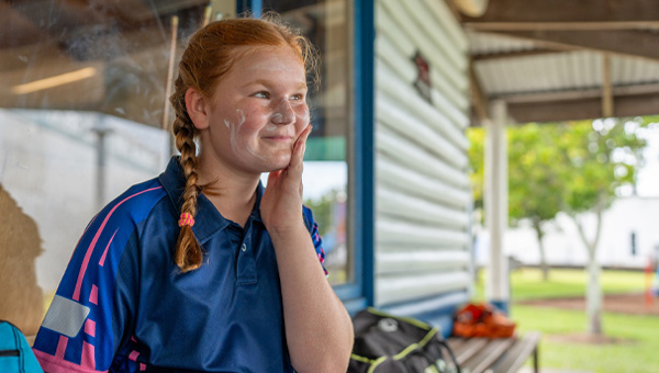 A young girl applies suncream to her face at school.