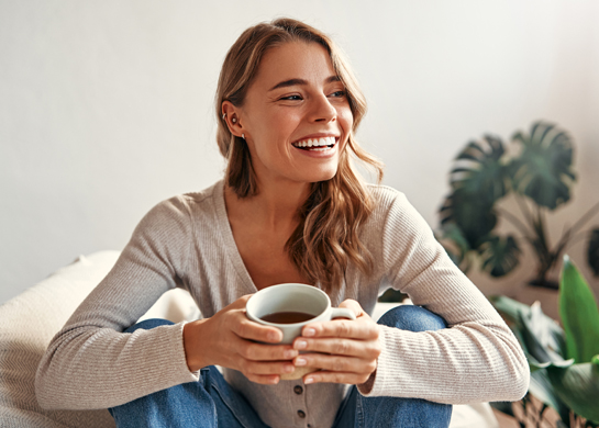 A woman drinks coffee while sitting on the couch.