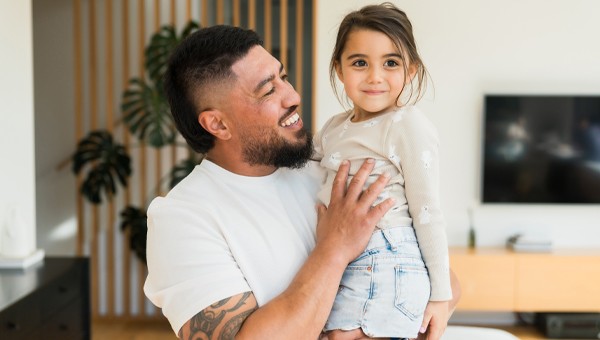 A young father cuddles daughter in the loungeroom.