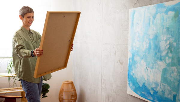 A woman looks at a painting before she hangs it.