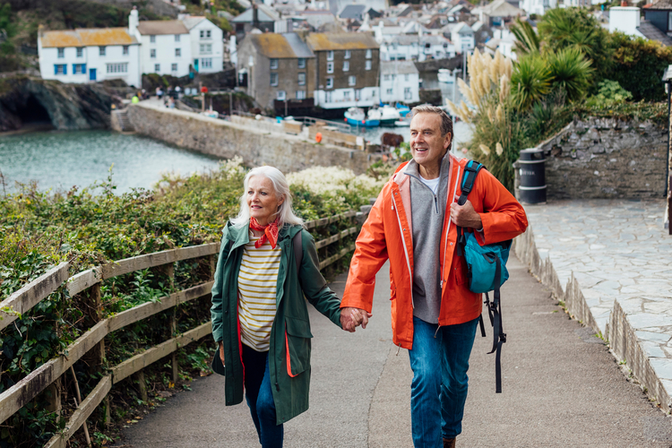 Older couple on vacation in a seaside town, holding hands as they walk up a path.