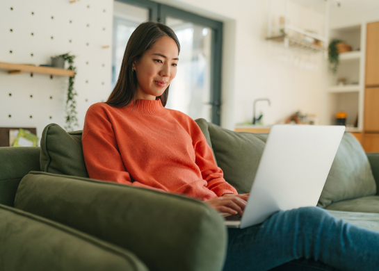 A woman reclines on a green sofa with her laptop.
