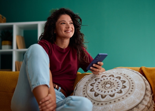 Woman sits on her couch with a cushion holding her phone.