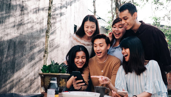 A group of friends look at something on a phone and are laughing.