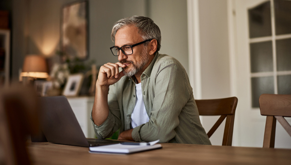 A man using a laptop at the dining room table.