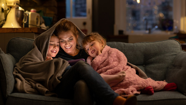 A mother and her kids watch a tablet under a blanket