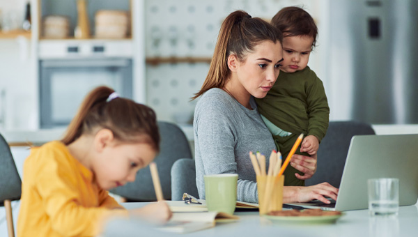 Mother uses laptop with kids at the dining room table.