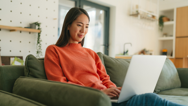 A woman reclines on a green sofa with her laptop.
