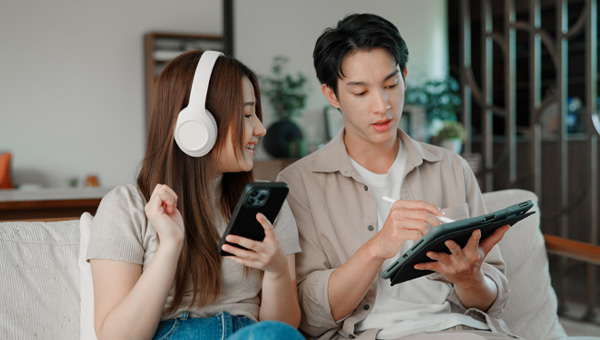 Woman uses her phone while her partner uses a tablet. They are sat on the couch.