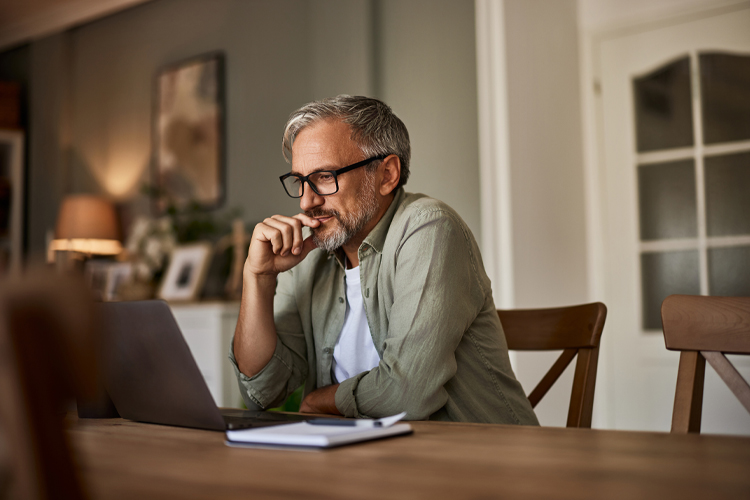 A man using a laptop at the dining room table.