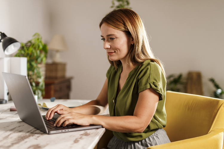 Woman sits at a marble table using her laptop.
