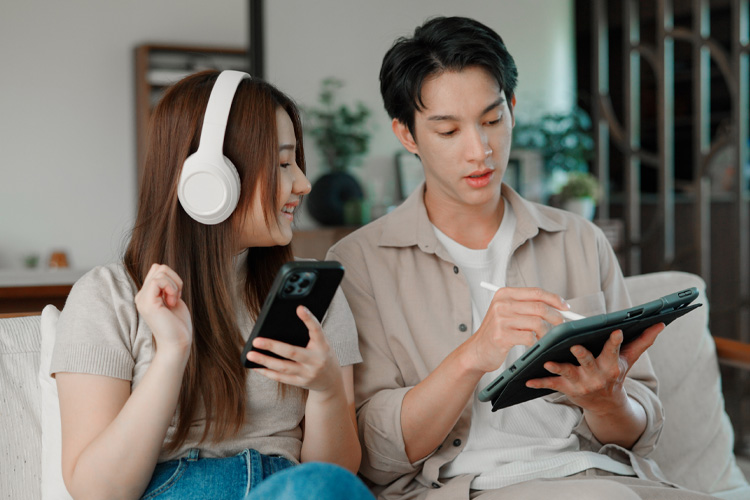 Woman uses her phone while her partner uses a tablet. They are sat on the couch.
