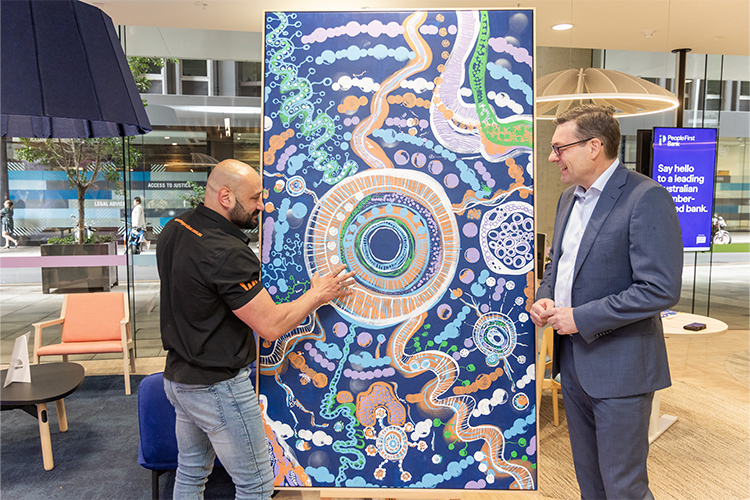 Eastern Arrernte Artist, Pat Caruso gesturing at his New Beginnings artwork while speaking to People FIrst CEO, Steve Laidlaw. 